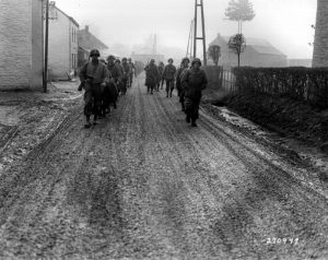 "U.S. troops of the 28th Infantry Division, who have been regrouped in security platoons for defense of Bastogne, Belgium, march down a street. Some of these soldiers lost their weapons during the German advance in this area. Bastogne, Belgium (12-20-44)." Source: U.S. Army Center of Military History: http://www.history.army.mil/html/reference/bulge/images/SC270947s.jpg. 