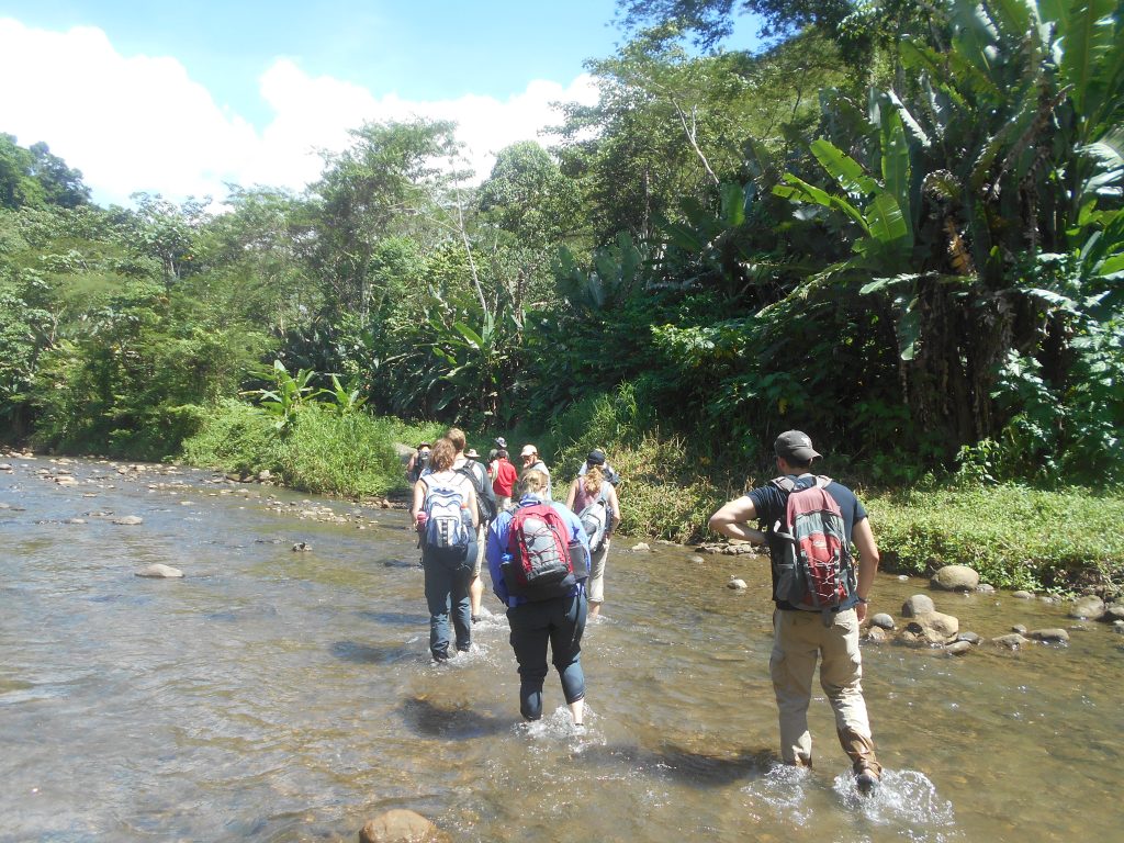 Students trek through a river to get to a waterfall