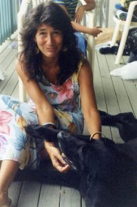 Photo of Dr. Gay Wilentz, seated on a grey deck with a black labrador. 
